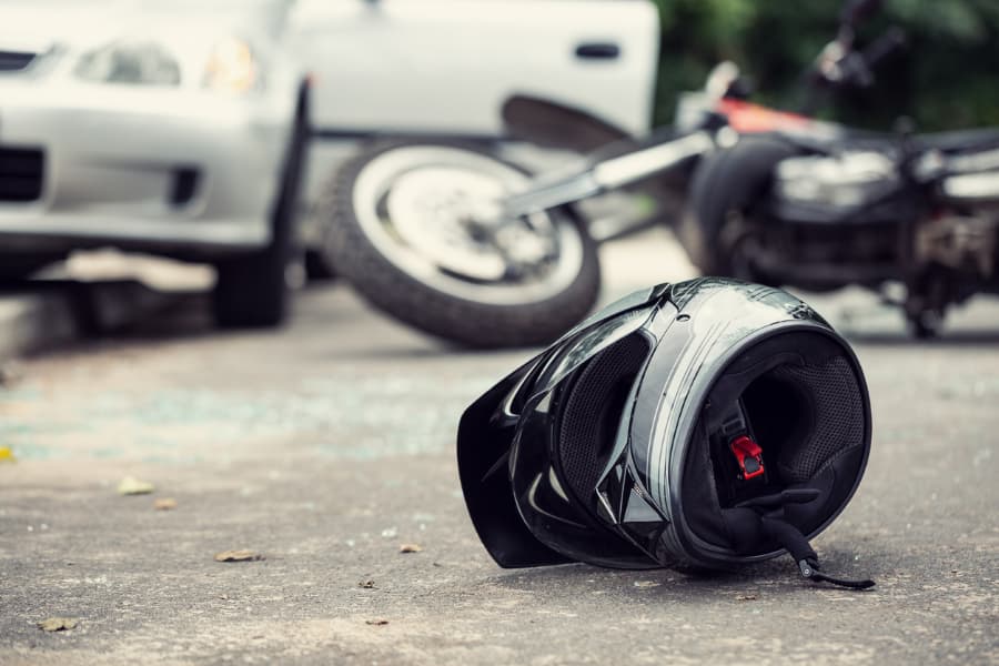 Blurred image of a silver helmet on the road with a wrecked motorcycle and car in the background