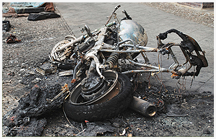 A wrecked, burnt motorcycle on the road after a crash
