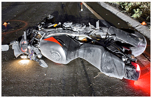 A wrecked motorcycle on its side on the road with lights shining