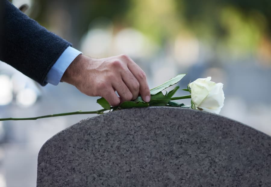 Close up of a man placing a white rose on a gravestone