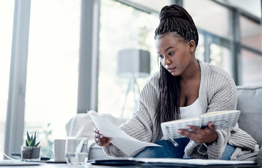 Shot of a young woman sitting on a couch going over insurance settlement