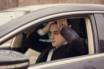 Distressed man sitting in car with hands on forehead