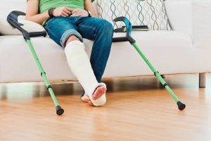 A man with a cast on leg sitting on a sofa with crutches next to him