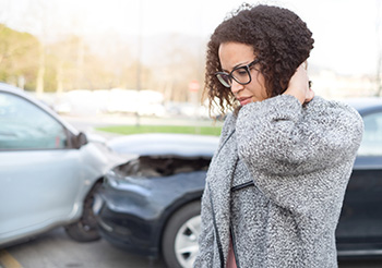 Woman holding her neck walking from a car collision in background