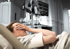 woman lying in hospital bed with hand over eyes