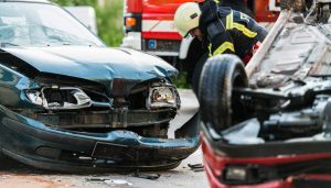 firefighter standing between two heavily damaged cars at an accident scene