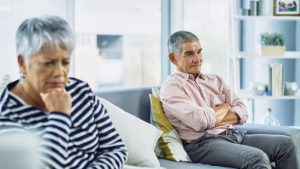 elderly man and woman on opposite ends of a couch looking frustrated