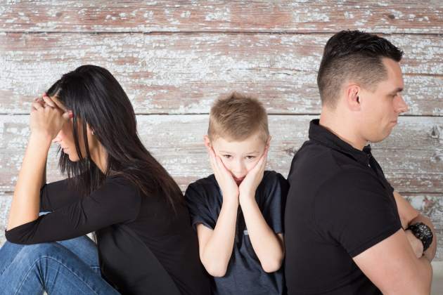 young boy with his head in hands sitting between his parents who aren’t facing each other
