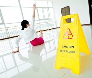 Businesswoman slips and falls on floor near a caution wet floor sign