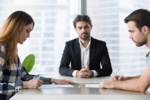 young couple sitting at table with lawyer signing divorce papers