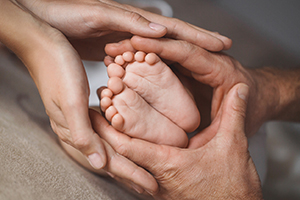 newborn baby’s feet surrounded by mom and dad’s hands