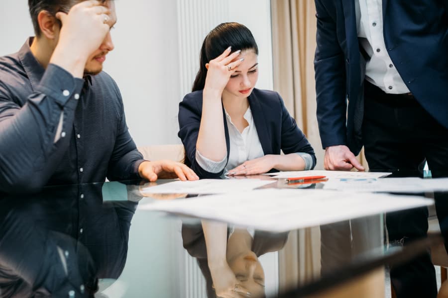 a distraught couple sitting at a table with many forms and a lawyer present