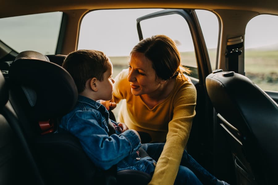 a mom greeting her son who’s sitting in the back seat of a car