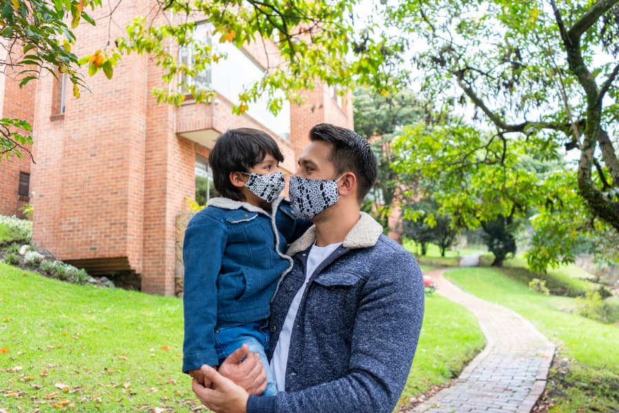 Father carrying son outside, wearing cloth masks