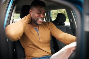 man sitting in car holding his neck with air bag deployed