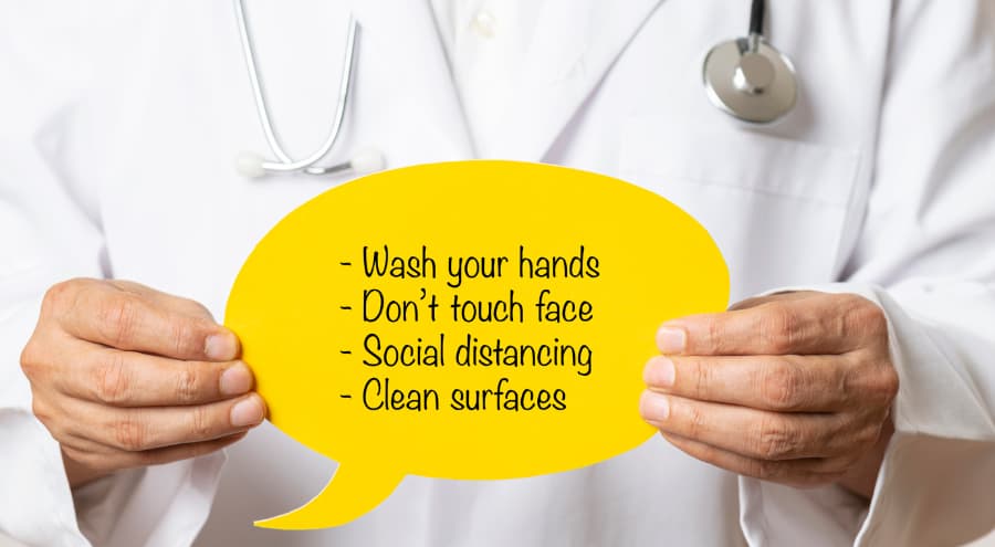 doctor holding a sign that says wash hands, don’t touch face, social distancing, and clean surfaces