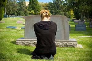 woman dressed in black kneeling in front of gravestone