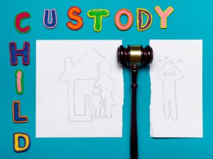 a family drawing torn in half with a judge’s gavel in the middle and colorful child custody letters beside and above it