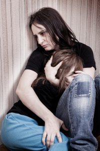 battered woman sitting on the floor holding her young daughter