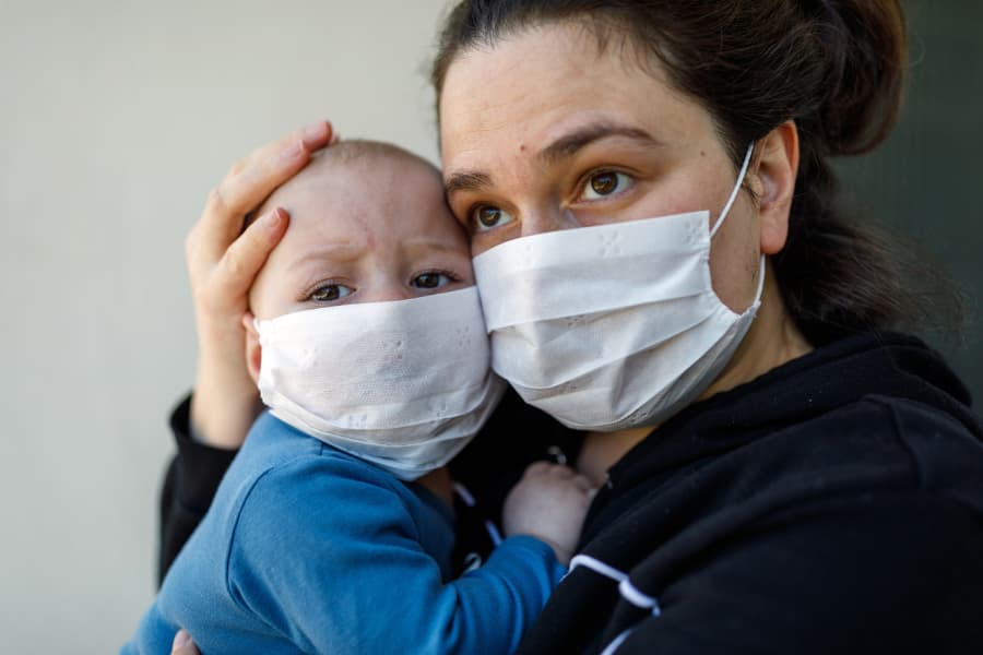 Mother holding baby, both wearing protective masks