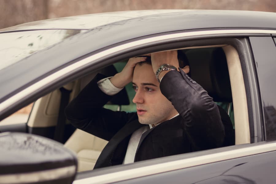 distressed young businessman sitting behind the wheel with hands on head