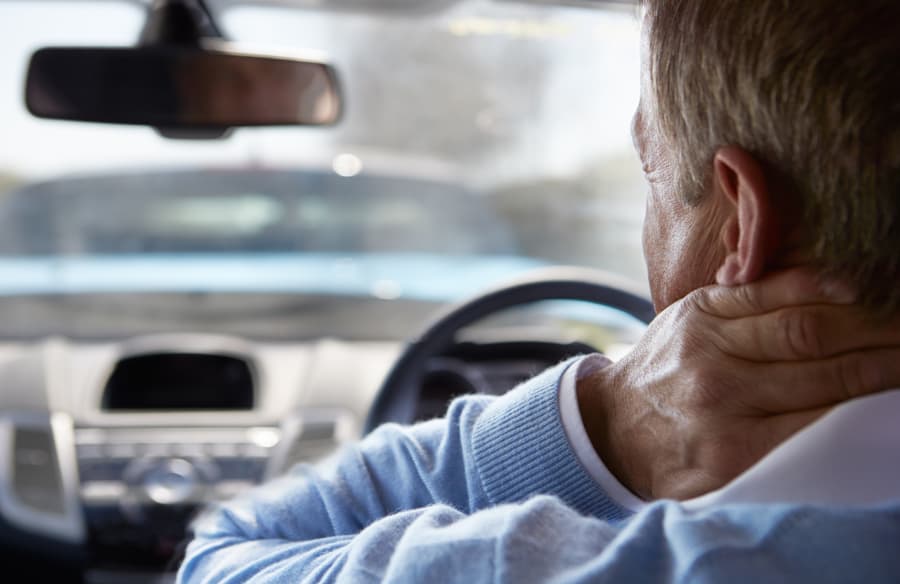 man sitting in his car holding his neck