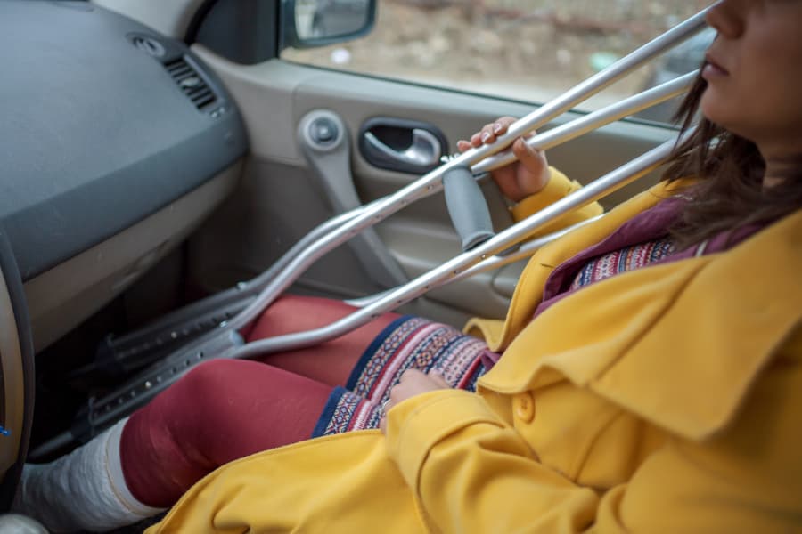 woman holding crutches while sitting in passenger seat with a leg cast