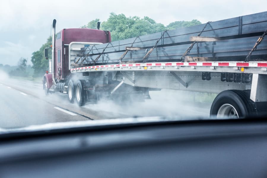 view from a car windshield of an 18-wheeler flatbed trailer truck on a rain-soaked highway