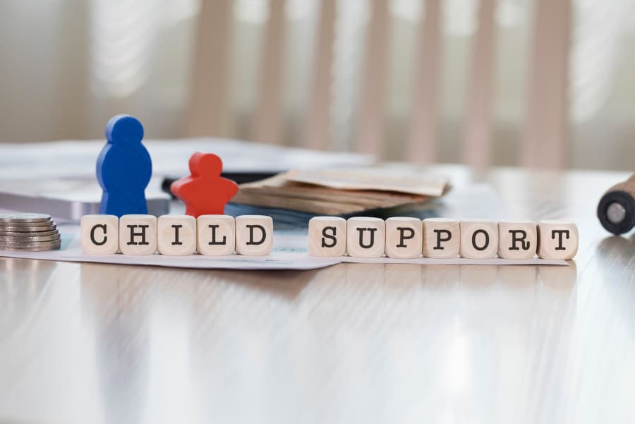 Wooden representation of child and parent behind blocks spelling CHILD SUPPORT