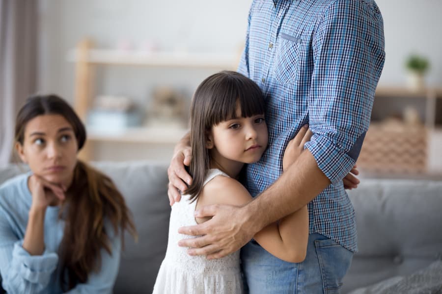 Daughter hugging father sadly as mother looks on