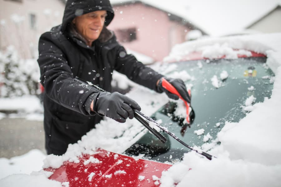 Man clearing snow from car windshield