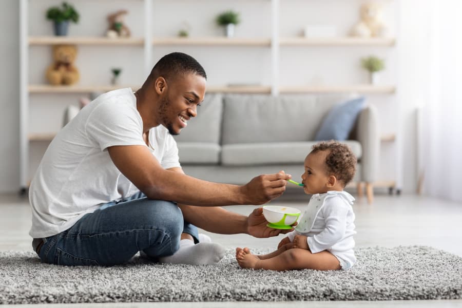 Smiling Father Feeding Baby On Floor