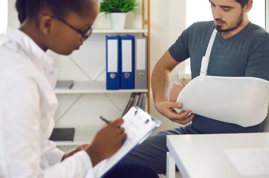 A man with an injured arm in a sling talks with a doctor