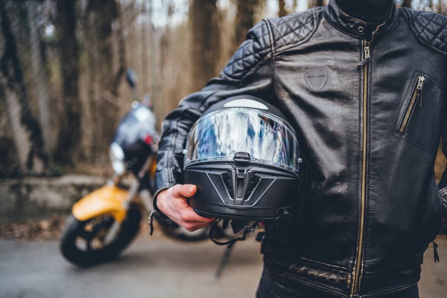 A motorcyclist in a leather jacket, holding a helmet