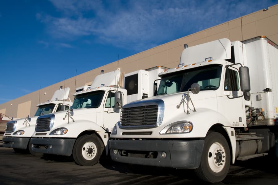 Three white semi-trucks lined up at the loading dock