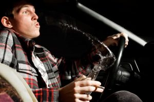 A man spilling a beer while driving drunk