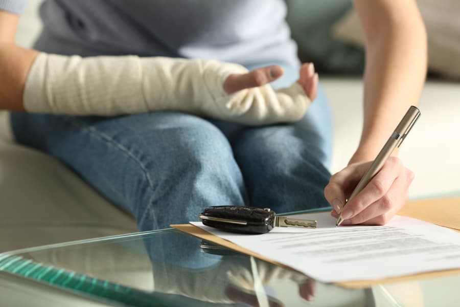 Close-up of a woman with a broken arm signing an insurance document after a car accident