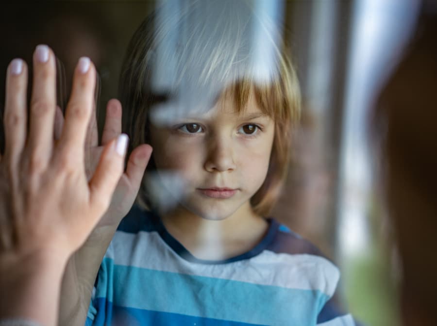 Sad boy looking through glass, talking to mother during visitation