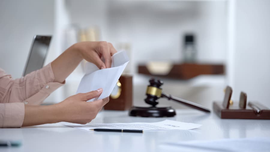 Woman holding spousal support envelope with paper, pen, and gavel in background