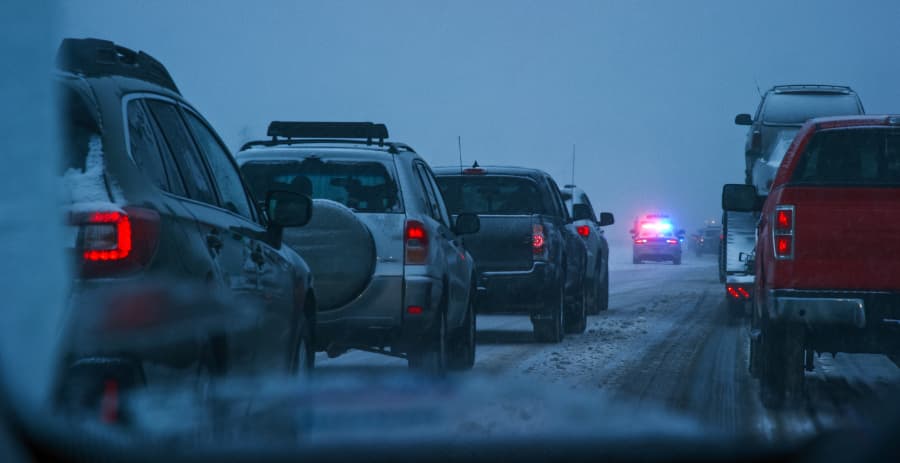 Vehicles stopped on the interstate during a snowstorm with a police car in the background