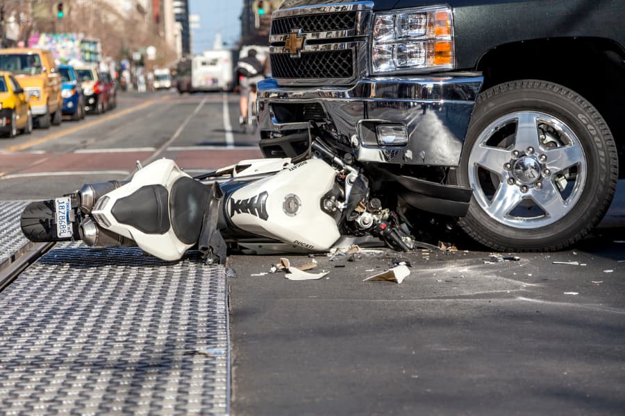 A damaged white motorcycle hit by a black SUV at an intersection