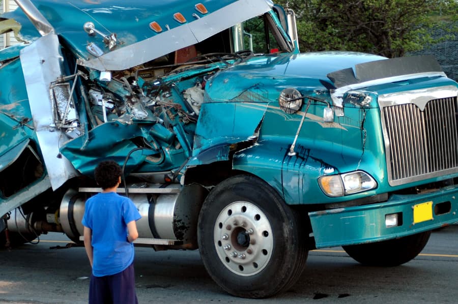 A young boy in front of a wrecked blue tractor trailer 