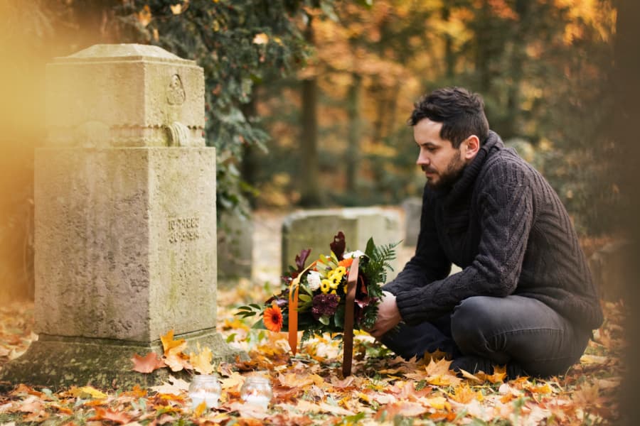 Man holding flowers sitting in front of a grave 