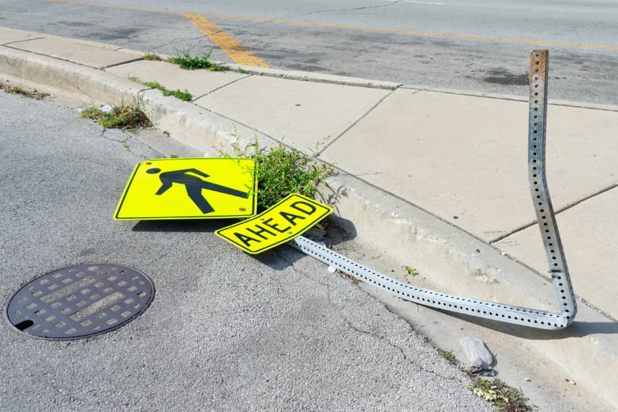 A damaged pedestrians ahead sign lying on the sidewalk