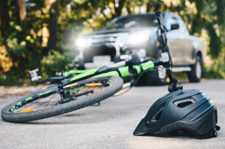 Close-up of a green bicycle and black helmet on the road with a truck in the background after an accident