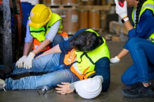 An injured warehouse worker with his foot stuck under a forklift being assisted by two coworkers