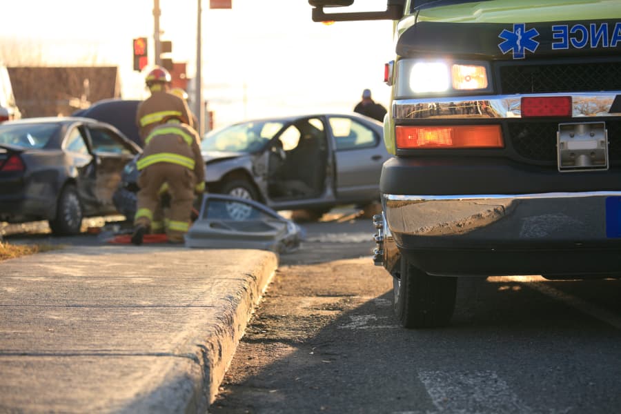 Auto accident scene with two firefighters assisting and a close-up of an ambulance in front