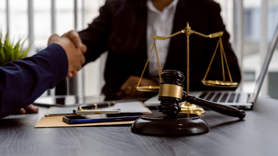 Close-up of a car accident attorney and clients shaking hands at a desk with a gavel and scale of justice in the foreground