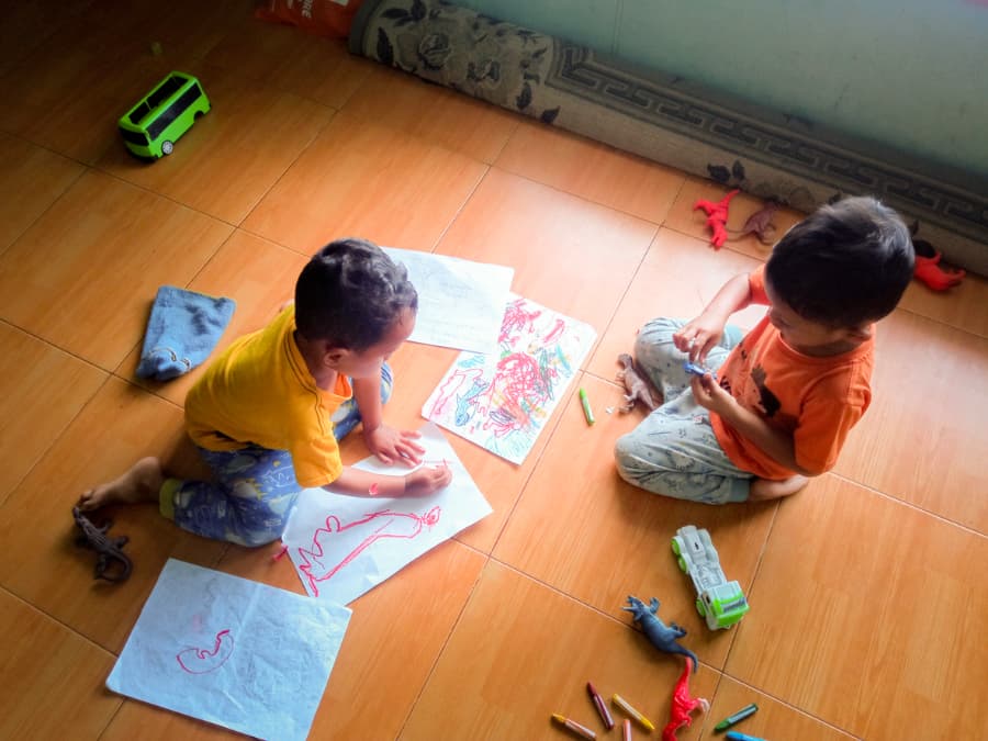 Two young children sitting on a wood floor drawing and playing 
